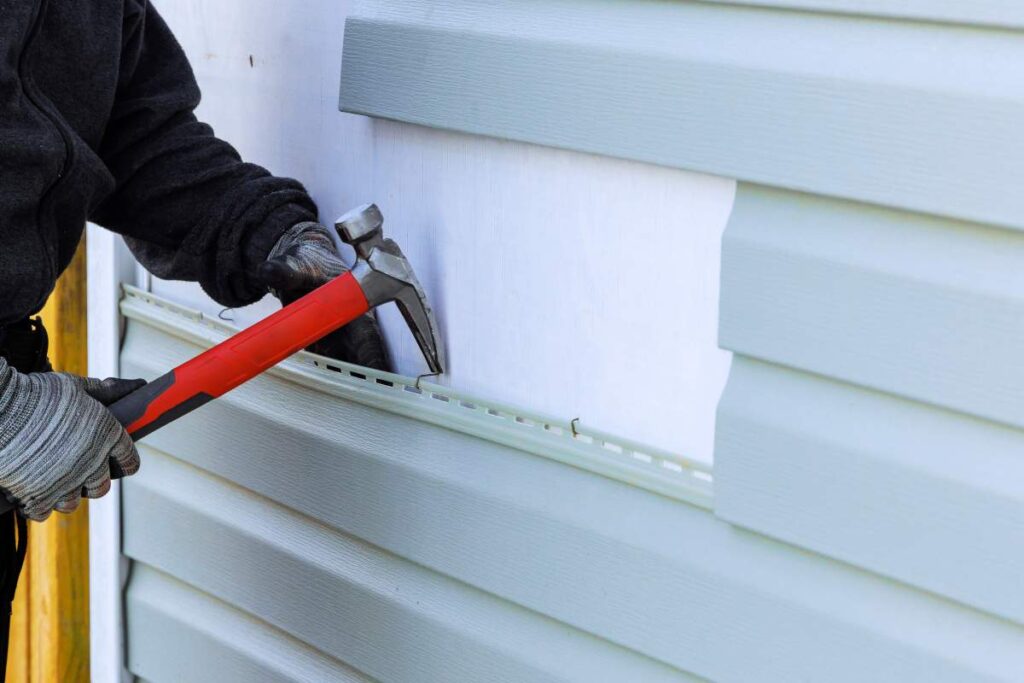 Homeowner sweeping leaves from a wooden deck beside outdoor stairs during autumn.