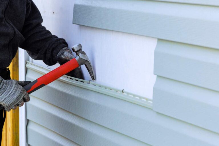 Homeowner sweeping leaves from a wooden deck beside outdoor stairs during autumn.
